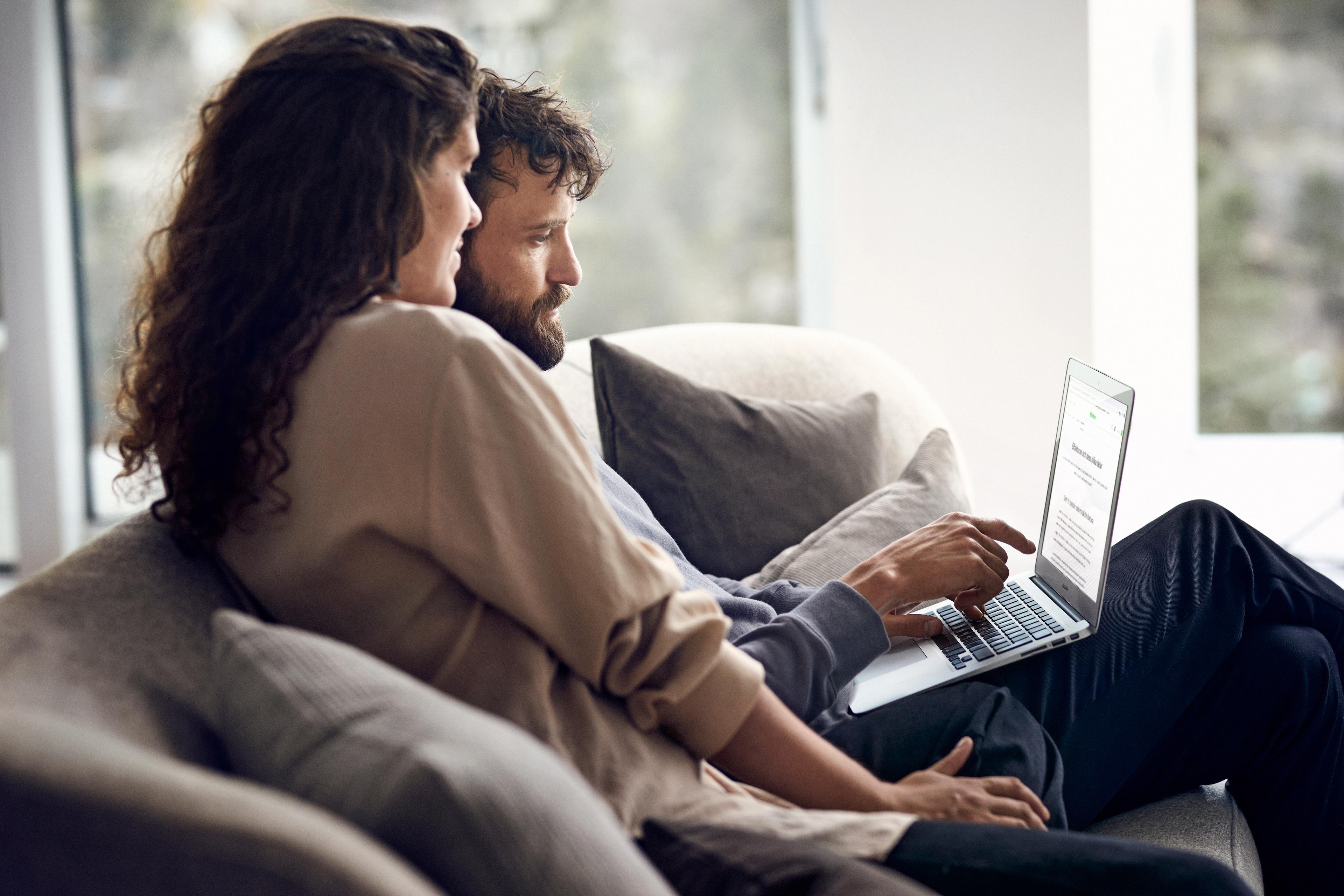 Man och kvinna sitter nära varandra i en soffa och tittar och pekar på skärmen till en laptop