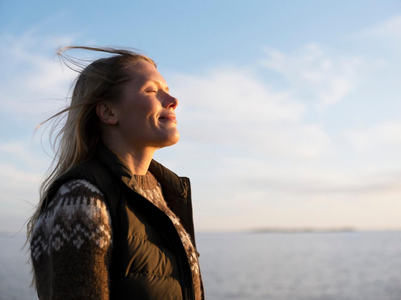 Kvinna ler och solar vid havet - teckna elavtal