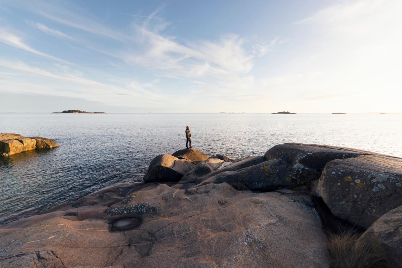 Person står på klippor vid Östersjön och ser ut över solnedgången